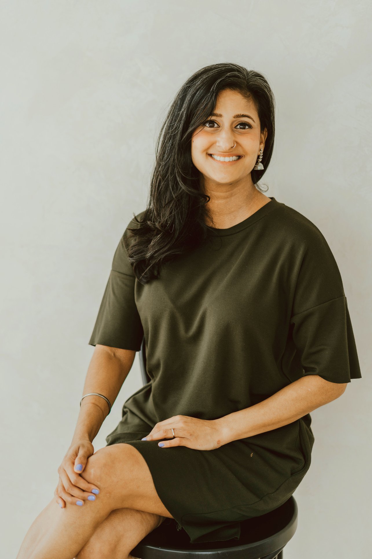 Sandeep is wearing a green dress and sitting on a stool in front of a white wall