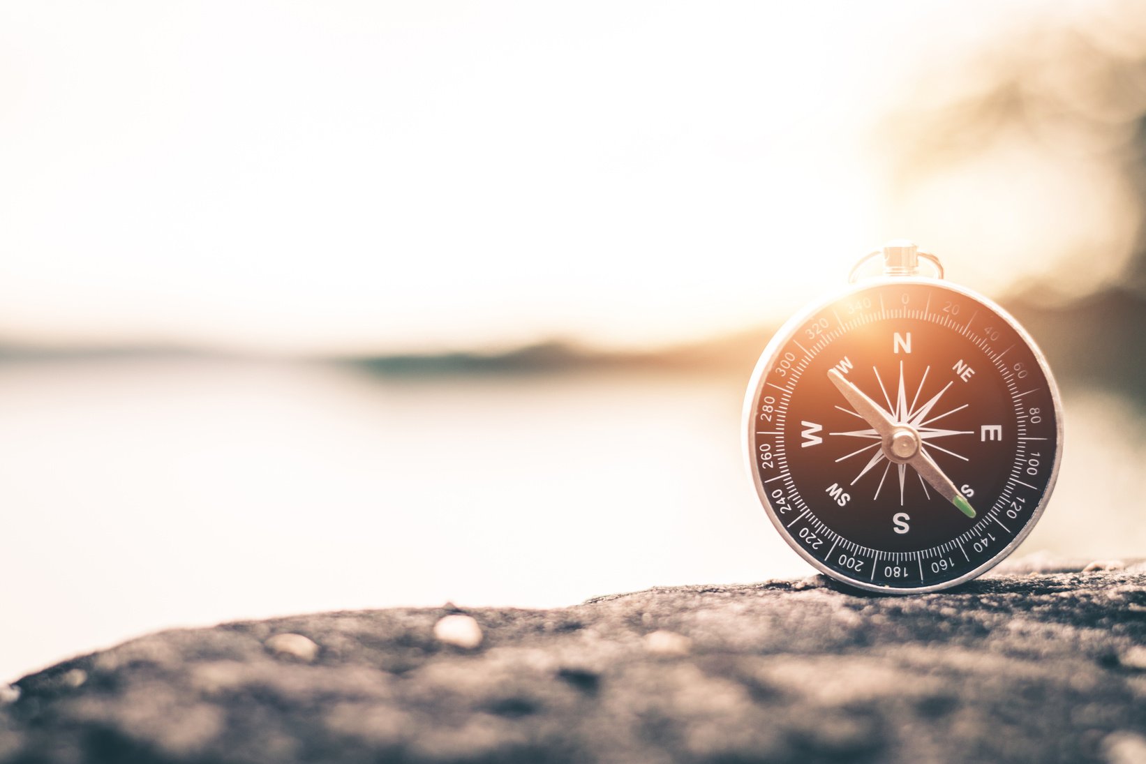 A compass sits on top of a rock with the sun in the background.